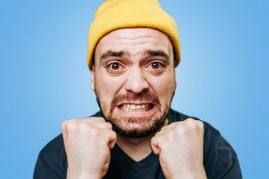 Heyecanlı bir çılgınlığın ortasında kalan bir adamın yakın plan portresi doğrudan kameraya bakarken yüzünde çılgın bir ifade beliriyor. Mavi arkaplanda stüdyo çekimi,