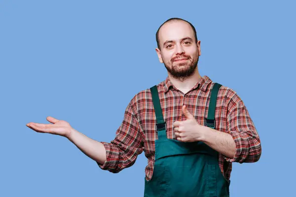 stock image A young man with a thumb up and an outstretched hand, expressing his happiness and delight in the studio against a blue background. copy space, Happy expression on a young male workman