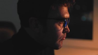 Eye on the Prize Close up of a male traders face, illuminated by the computer screen as he studies market trends. Wearing eyewear in the dimly lit room, he is fully invested in his work.