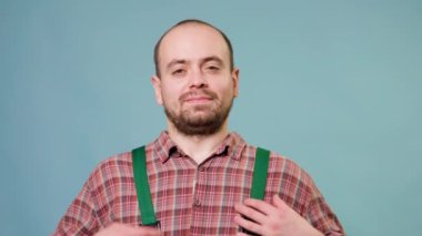 Mavi stüdyo arkaplanındaki kameraya bakan genç, yakışıklı adam saf bir mutluluk anında görüntülenir, yüzü parlak bir gülümseme ve keyifli bir ifadeyle ışıldar. Boşluğu kopyala
