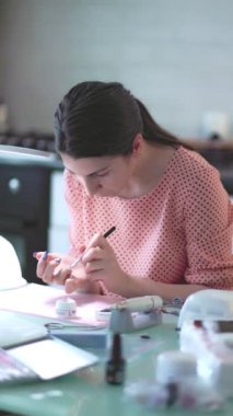 Genç bir kadın evde kişisel bakıma ilgi duyuyor, titizlikle manikürcünün uzmanlığı altında özel jel cilasıyla tırnaklarını boyuyor. dikey çekim