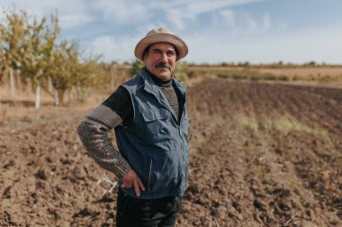 Esansı yakalamak, deneyimli bir kıdemli çiftçinin heybetli portresi, bilgeliği ve deneyimi somutlaştırmak, geniş bir tarım alanının pitoresk zeminine karşı kuruludur..