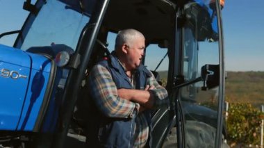 İnsan ve makine arasındaki ahenge tanık olun, kıdemli bir çiftçi, üretkenliğin ve tarım arazisindeki ilerlemenin bir sembolü olan traktörünün yanında poz verirken,.