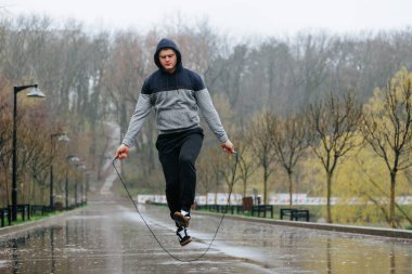 Yağmurda Atlayan Atletik Adam. Yağmurlu günler atletizm eğitimini durdurmayacak. Buna kardiyo ve dayanıklılık için ip atlamak da dahil..