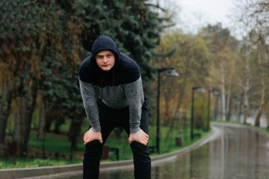 Yorgunluğun üstesinden gelen genç bir adam, eğitiminde yağmuru zorluyor. Bir Sporcunun Yağmurdaki Beyaz Atlet Portresi 'nin Dayanıklılığı