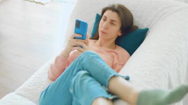 Esmer bir kadın evinde boş bir anın tadını çıkarıyor. Kanepede oturuyor ve akıllı telefonuna tatmin olmuş bir ifadeyle bakıyor..