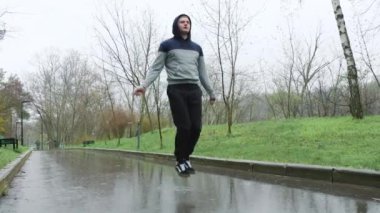 Yağmurlu bir günde erkek sporcu ip atlama açık havada. Yağmura rağmen, bu adam kendini tamamen fiziksel eğitimine adamış. Zorlu ve etkili bir egzersiz seansı için ip atlıyor..