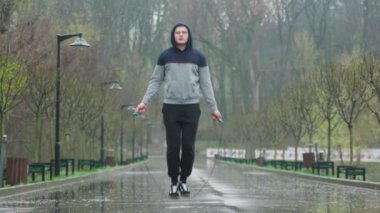Yağmurlu bir günde erkek sporcu ip atlama açık havada. Yağmura rağmen, bu adam kendini tamamen fiziksel eğitimine adamış. Zorlu ve etkili bir egzersiz seansı için ip atlıyor..