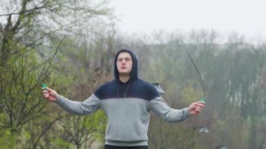 Yağmurlu bir günde erkek sporcu ip atlama açık havada. Yağmura rağmen, bu adam kendini tamamen fiziksel eğitimine adamış. Zorlu ve etkili bir egzersiz seansı için ip atlıyor..