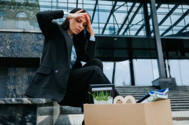 An employee sits on a cardboard box, holding a lossjob notice and looking worried and upset about their future job prospects. clipart