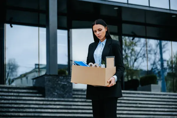 stock image The Emotional Burden of Unemployment. A female worker holds a cardboard box, visibly distressed after losing her job due to workloss and unemployment.