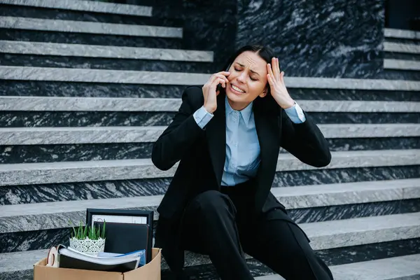 stock image jobless person feeling anxious and upset while talking on the phone and holding a mobile phone while sitting on the stairs. Sitting on Stairs Woman on Phone Discussing Job Loss and Workless Situation