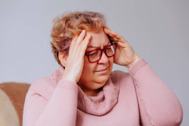 Stresli, son sınıf öğrencisi, elleriyle başını tutarak oturma odasında sürekli baş ağrısı çeken, evde migrenden muzdarip yaşlı bir kadın.