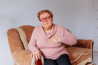 Overweight distressed Senior Woman Suffers Heart Attack on Sofa at Home , This photo shows a woman who is overweight and a senior, experiencing a heart attack while sitting on her sofa at home