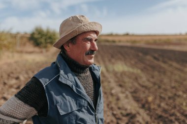 Bu dokunaklı resimde, yaşlı bir çiftçi portresi, onun tarım alanının bereketli manzarasıyla çevrili bir adanmışlık ve dayanıklılık hikayesi anlatıyor..