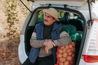 Hasat zamanı kıdemli çiftçi, patates çuvallarıyla çevrili bir aracın yanında dinleniyor. Hasat zamanı tarımsal işçilikte kısa bir ara veriliyor..