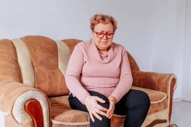 Bacak Ağrısının Üstesinden Gelen Yaşlı Bir Kadın Eve Yolculuk, Yaşlı bir kadın evinde dinlenirken bacak ağrısı yaşıyor, kilolu vücudunun rahatsızlığından açıkça muzdarip.