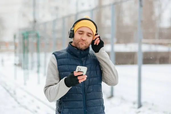 stock image Winter A man enjoys the beauty of winter while indulging in music, his headphones and smartphone in hand. Music in Motion Guy Jogging with Headphones in Wintertime
