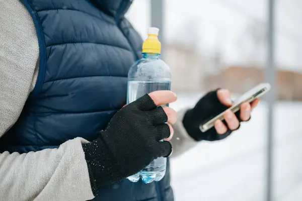 Stock image close up view of two gloved male hands with water bottle and smartphone in winter time