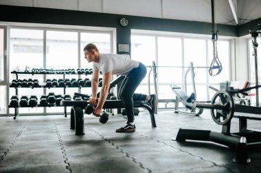 A young, active caucasian male athlete performing a weightlifting exercise with determination in the gym. Young caucasian male athlete performing intense weightlifting workout in the gym clipart