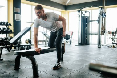 Kendini işine adamış bir erkek sporcu, gücünü ve kararlılığını gösteren titiz bir halter figürü sergiliyor. Enerjik genç adam spor salonunun bir parçası olarak ağırlık kaldırıyor.