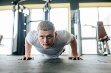 Aktif bir Kafkas erkeği, kapalı spor salonunda fitness rejiminin bir parçası olarak zorlu bir şınav egzersizi yapıyor. Yakışıklı görünüşü ve kararlılığıyla,