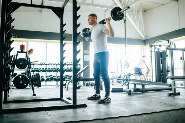 Stock image A determined young man performing an intense workout with a barbell in the gym, focusing on his physical strength and endurance. Strength Unleashed Man Exercising with Barbell in the Gym