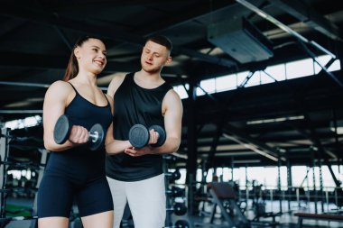 Spor salonunda, yetenekli bir erkek özel antrenör, bir kadına halter egzersizinde yardımcı olur. Eğitimini en üst seviyeye çıkarmasını sağlar. Spor Eşleri Erkek Eğitmeni Salağın Kaldırılmasına Yardım Ediyor
