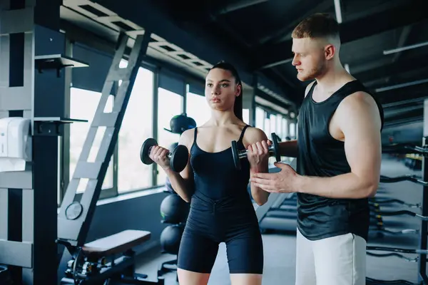 stock image In the gym, a dedicated male personal trainer acts as a coach, offering encouragement and support to a woman during her dumbbell lift. Personalized Coaching Male Personal Trainer Supports Woman in Gym