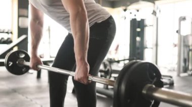 Spor kıyafetleri giyen genç bir adam, yüksek yoğunluklu halter egzersizi yapıyor, aktif ve formda bir yaşam tarzına bağlılığını gösteriyor..