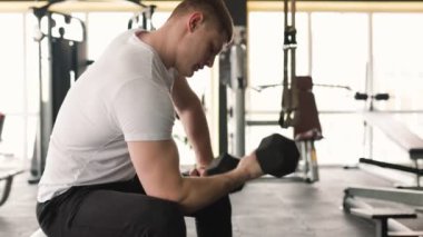 Spor salonundaki halter egzersizinde kendini spora adamış genç bir adam açıkça görülüyor. Tutkulu erkek fitness meraklısı kendini fiziksel eğitimine adamış, kendini zorluyor.