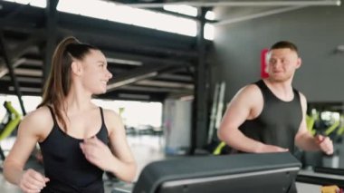 Beyaz bir erkek antrenör, spor salonundaki yüksek yoğunluklu egzersiz sırasında genç bir İspanyol kadına rehberlik ediyor. Spor salonunda Erkek Özel Eğitmeniyle Koşan Aktif Genç Kadın