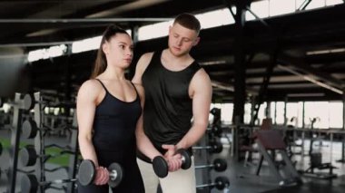 Erkek kişisel antrenörün de desteğiyle bir kadın spor salonunda halterini rahatça kaldırır. Dumbbell Egzersiz Erkek Antrenörü Kadın Antrenmanlarını Destekliyor