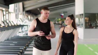 Kendini adamış bir erkek özel antrenör, bir kadınla bir konuşma yapar, antrenman sırasında uygun form ve tekniğin önemini vurgulayarak, etkili ve güvenli çalışmalar sağlar..