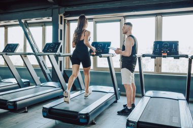 Motive olmuş genç bir kadına birebir fitness eğitimi veren, fiziksel gücünü ve dayanıklılığını geliştirmesine yardım eden beyaz bir erkek antrenör..