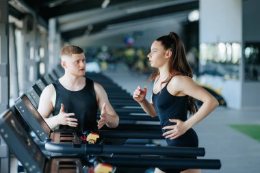 Bir erkek eğitmen tarafından yönetilen bir grup erkek ve kadın spor salonunda genel fitness seviyelerini yükseltmek için yoğun bir antrenmana katılıyorlar..