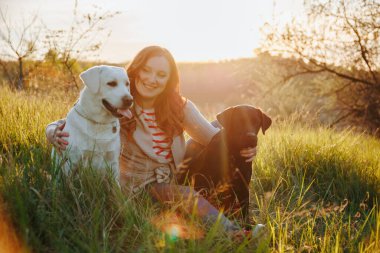 Kadın ve labradoru gün batımında doğanın güzelliğini kucaklıyor. Kadınların evcil köpekleriyle keyifli etkileşimleri