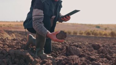 Deneyimli kıdemli bir çiftçi, bıyıklı, hasat sırasında dijital tablet kullanıyor. Uzmanlığı eski bilgeliği modern teknolojiyle harmanlıyor, ekin koşullarını optimize ediyor..