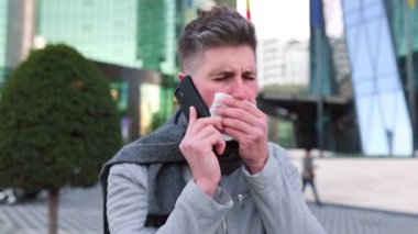 Genç adam akıllı telefon kullanıyor ve şehirde hapşırıyor.