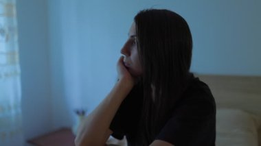 Yatak odasının yalnızlığında, genç bir kadın yatağında oturur, yüzü hüzün ve yorgunlukla işaretlenmiştir. Yalnızlığın ve depresyonun karşı konulmaz duygularıyla savaşıyor..