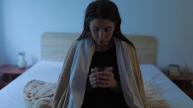 Ateşi olan bir kişi gece yatakta dinlenirken, hasta ve rahatsız hisseder. Yatak odasının yanında bir bardak su ve ilaç var.,