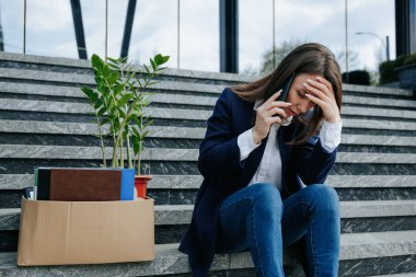 Mutsuz bir kadın merdivende oturuyor, cep telefonuyla depresyondaki durumu, işsizliği ve işini kaybetmesi hakkında konuşuyor. Smartphone 'da İş Kaybı ve İşten Çıkarma Hakkında Konuşan Kadın