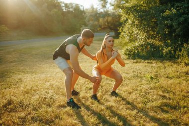 Bir atletizm ruhu antrenörü, erkek sporcu ve bayan sporculara açık havada yaptıkları antrenman sırasında sarsılmaz bir destek sağlıyor ve adanmışlığın önemini vurguluyor.