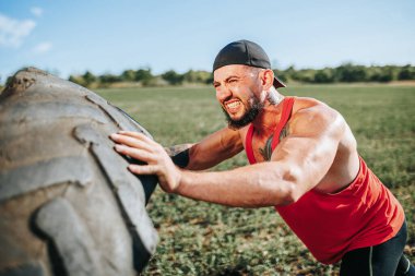 Bu CrossFit antrenmanında güçlü bir erkek sporcu var. Yetenekli ve zorlu bir tekerleği kaldırırken kaslı fiziğini ve azmini gösteriyor..