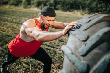 Açık havada yapılan CrossFit antrenmanında kaslı bir adam limitlerini zorluyor, kendini spora adamış ve kendini spora adamış bir tekerleği kaldırıyor..