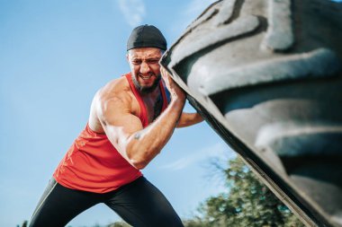 Bu CrossFit denen adam açık hava antrenmanında azim ve gücü gösteriyor. Spor yolculuğuna sarsılmaz bir bağlılıkla bir tekerleği kaldırıyor..
