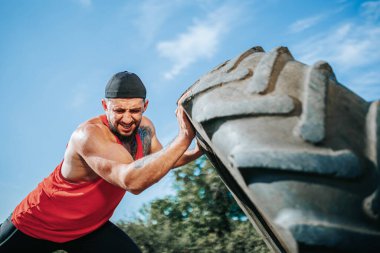 Bu CrossFit 'in gücünü ve kararlılığını gözlemleyin. Açık havada antrenman yapıyor. Dikkate değer bir güç ve kontrolle tekerleği kaldırıyor..