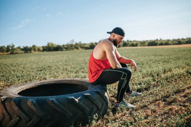 Güçlü bir kararlılığa sahip kaslı adam CrossFit tekerleğinin orada mola veriyor. Etkin Açık Hava Çapraz Sığdırmalı Güçlü Erkek Sporcu Dinleniyor