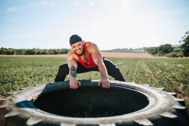 Güçlü bir erkek sporcu, CrossFit tekerleğini dışarı çeker ve fiziksel forma olan bağlılığını gösterir. Çapraz Fit Eğitim Oturumu Görevlisi Vitrinleri Dışarı Çekiyor