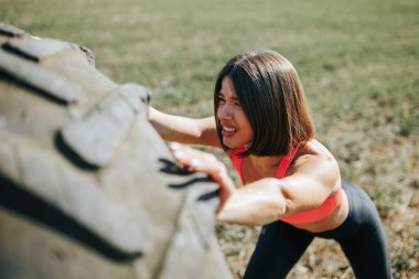 Çapraz Fit sporcusu dışarıda tekerleği kaldırırken güç ve güç gösteriyor. Kaslı Çapraz Fit Kadını Bir Tekerlek Kaldırma ile Açık Hava Çalışması Yapıyor